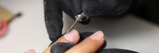 Nail master using tool to clean female clients nails in beauty studio