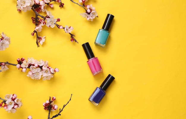 Nail pilish bottles and beautiful flowering branches on yellow background Springtime beauty concept Flat lay top view