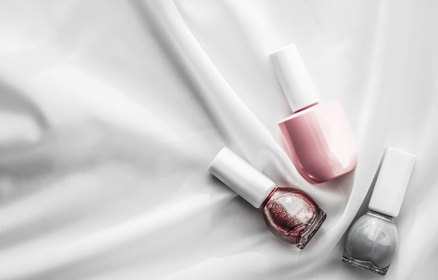 Bottiglie di smalto per unghie su fondo di seta prodotti per manicure francese e cosmetici per il trucco di smalto per il marchio di bellezza di lusso e design artistico flatlay per le vacanze