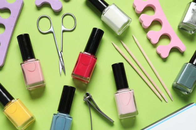 Nail polishes and set of pedicure tools on green background flat lay