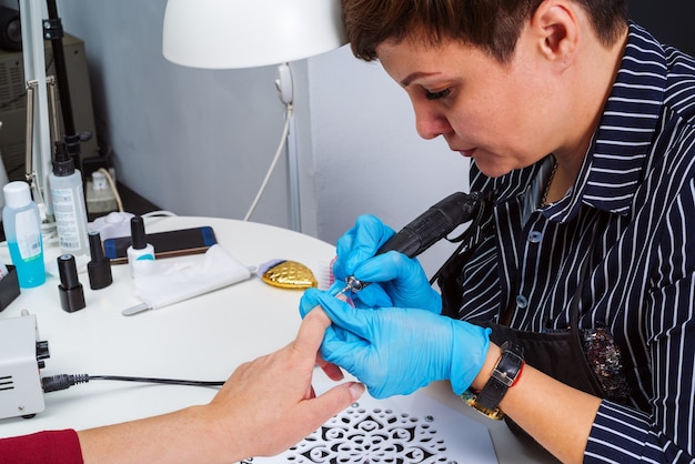 Nail salon, hands of client and master close-up. Nail treatment with a cutter