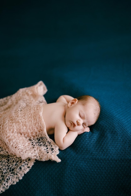 Naked baby covered with shawl sleeps on blanket