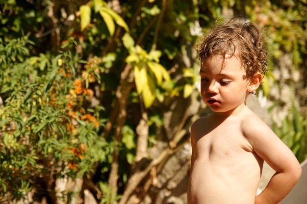 Naked boy looking away while standing at backyard