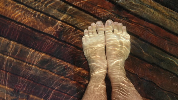 Naked hairy male legs walk on pier the legs of a man swim first person of view men rest on a flood wood underwater pier