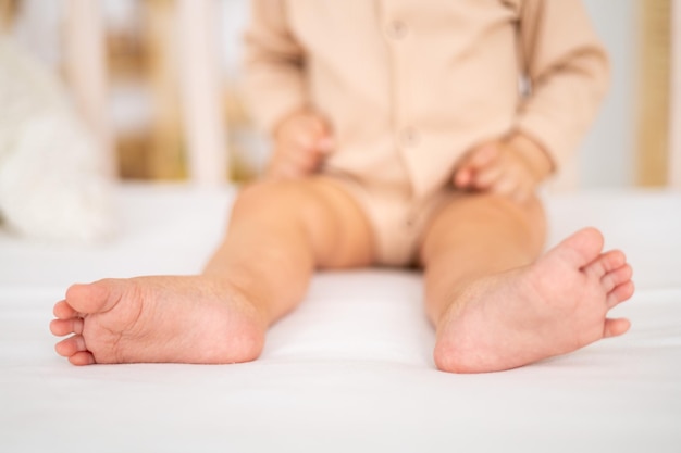 Naked healthy legs of a small child closeup on the background of a baby cot on white bed linen