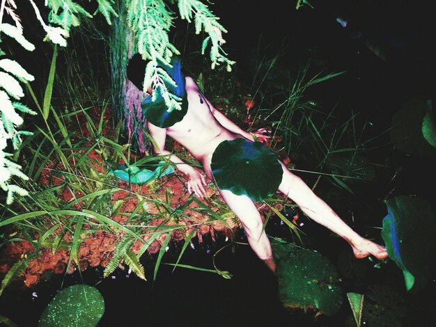 Naked man lying by pond amidst leaves at night