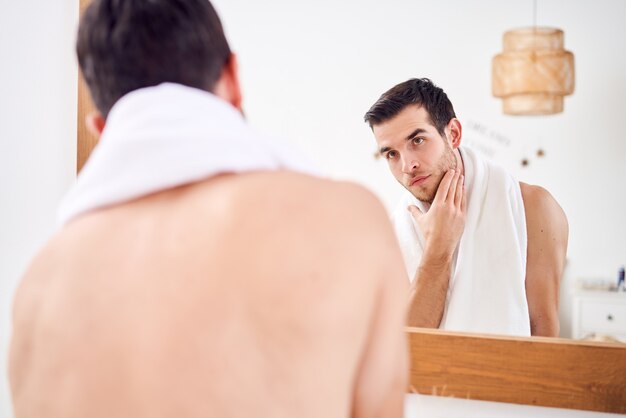 Naked man with white towel on his neck standing near mirror