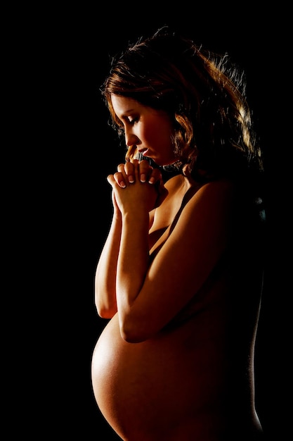 Photo naked pregnant woman with hands clasped standing against black background