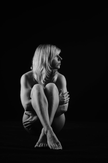 Foto donna nuda seduta su uno sfondo nero
