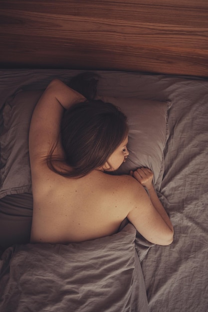 Naked woman sleeping in the bed with hand under pillow