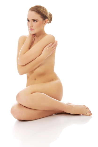 Naked young woman looking away while sitting against white background