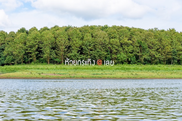 Табличка с именем Хуай Кратинг в Лое на травянистом холме у реки перед зеленым лесом - известная туристическая достопримечательность в Таиланде.