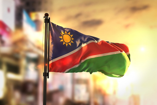 Namibia Flag Against City Blurred Background At Sunrise Backlight