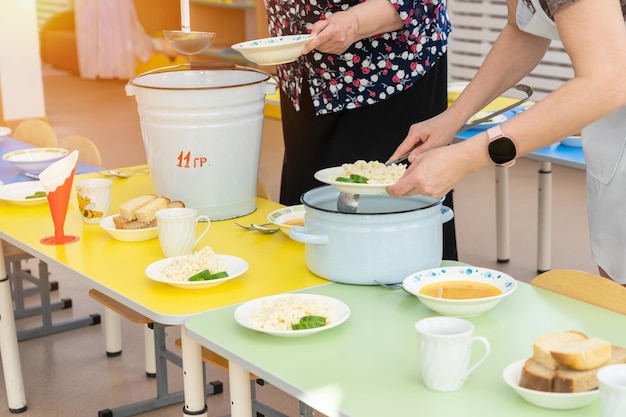 Nannies in kindergarten put food on plates and serve tables before lunch