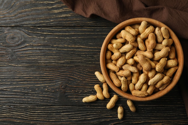 Napkin and bowl with peanuts on wooden background