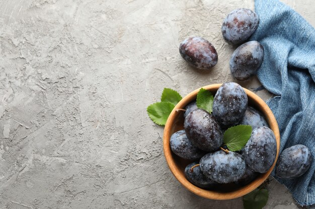 Tovagliolo e ciotola con prugne su grigio