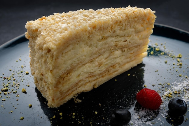 Napoleon cake on a dark plate with berries on dark concrete