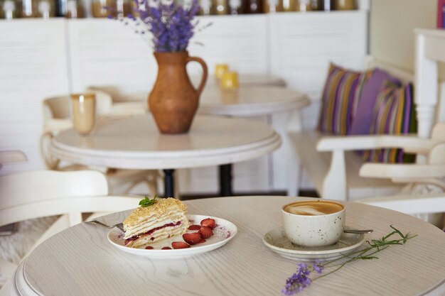 Napoleon piece of cake and cup of cappuccino on wooden table in the cafe Lavander in the jug Aesthetic coffee time Time for yourself