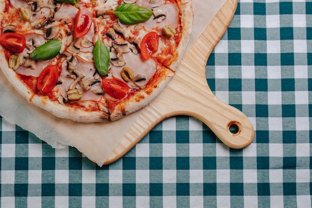 Napolitaanse pizza met champignons, kaas, rucola, basilicum, tomaten bestrooid met kaas op een houten bord