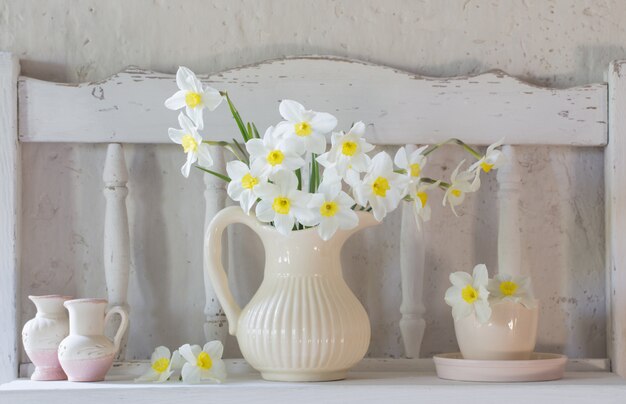 Narcissen in kruik op witte tafel