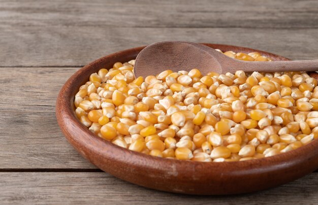 Узкий фокус, сушеная кукуруза или зерна попкорна в тарелке над деревянным столом.