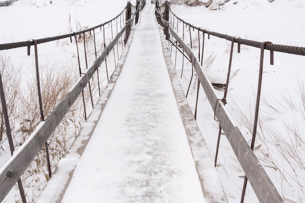 Narrow snow covered old bridge over frozen river