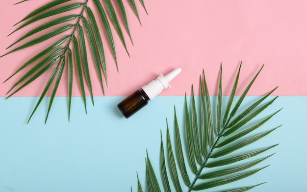 Nasal spray bottle and palm leaves on pink blue background Top view Flat lay