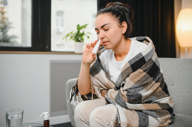 소파에 앉아 있는 아픈 젊은 여성의 손에 비강 스프레이 알레르기 비염 증상 및 치료