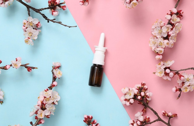 Nasal spray with beautiful flowering branches on pink blue background Springtime concept Flat lay top view