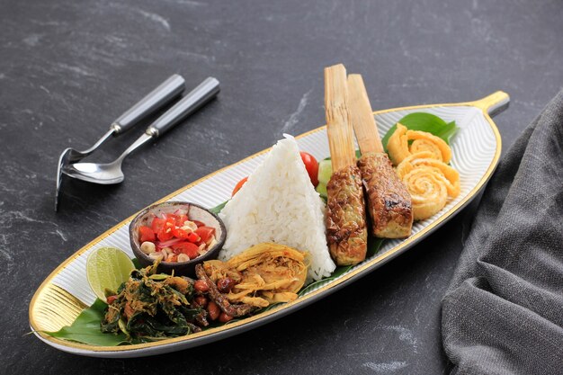 Nasi campur bali. popolare pasto balinese a base di riso con vari contorni, servito insieme. questo menu contiene ayam sisit, sate lilit, saute papaya leaf e sambal matah.