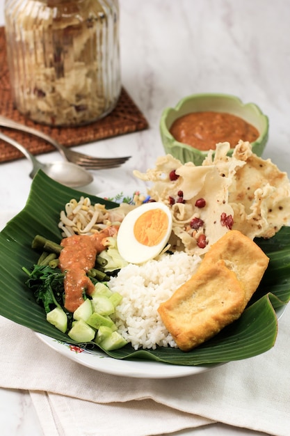 Nasi Pecel. Traditional Javanese Rice Dish of Steamed Rice with Vegetable Salad, Peanut Sauce Dressing, Tempeh, Tofu Beancurd, and Peyek Crackers. Pecel Madiun is Most Popular Variant