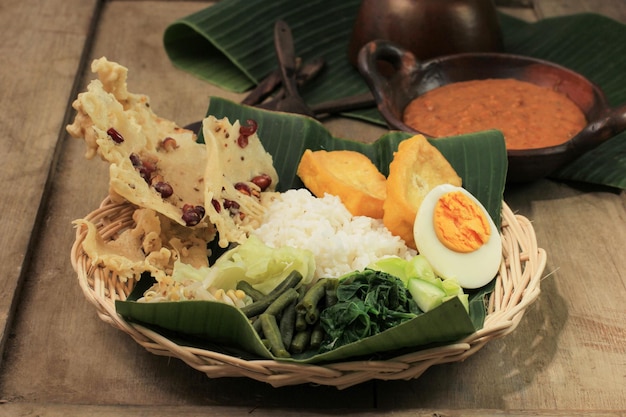 Nasi Pecel. Traditional Javanese Rice Dish of Steamed Rice with Vegetable Salad, Peanut Sauce Dressing, Tempeh, Tofu Beancurd, and Peyek Crackers. Pecel Madiun is Most Popular Variant