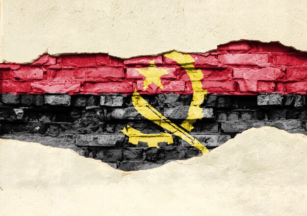 National flag of Angola on a brick background. Brick wall with partially destroyed plaster, background or texture.