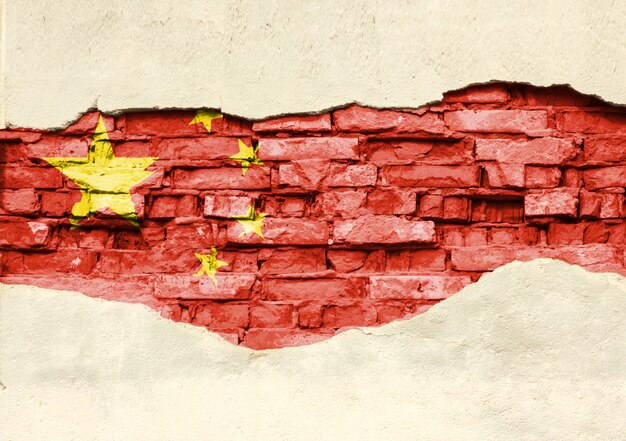 National flag of China on a brick background. Brick wall with partially destroyed plaster, background or texture.