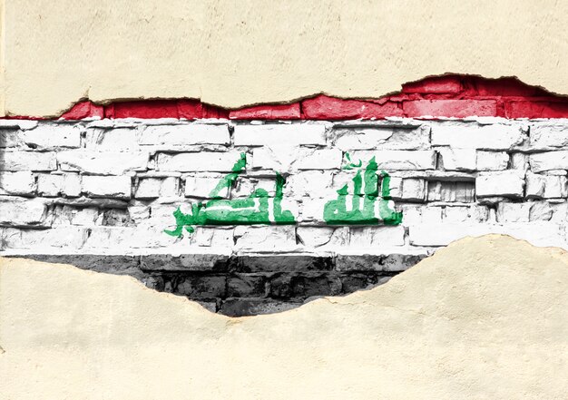 National flag of Iraq on a brick background. Brick wall with partially destroyed plaster, background or texture.