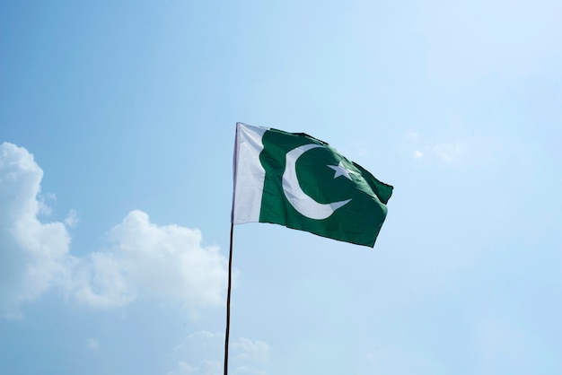 The national flag of Pakistan flying in the blue sky with clouds