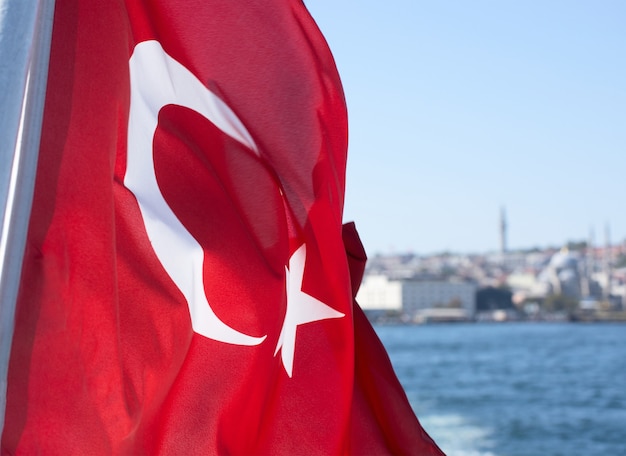 La bandiera nazionale della turchia contro le acque del bosforo e gli edifici della città di istanbul
