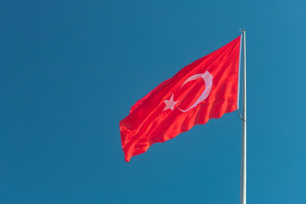 National flag of Turkey on a flagpole waving against a blue sky