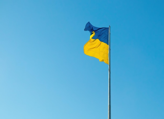 The national flag of ukraine flutters in the wind on a flagpole against a clear blue sky