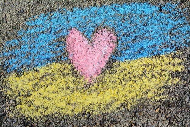 National flag of Ukraine with heart drawn by color chalk on asphalt top view