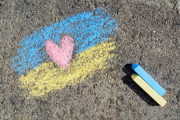 National flag of Ukraine with heart drawn by color chalk and sticks on asphalt flat lay