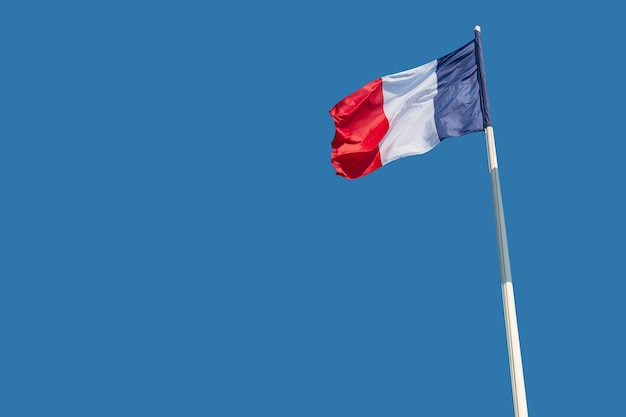 The national flags of France flutter against a blue sky