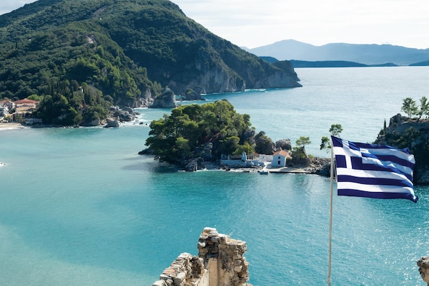 Bandiera nazionale greca che sventola sullo sfondo di una splendida vista sul mare, le montagne della baia di parga, il mare turchese con tempo soleggiatoviaggi in greciail pittoresco concetto di paesaggio marinovista dalla fortezza superiore