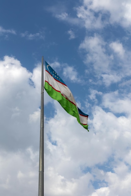 Государственный флаг Узбекистана развевается на ветру на фоне голубого неба с легкими облаками