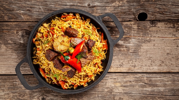 National Uzbek pilaf with meat in a cast-iron skillet, on a wooden table.