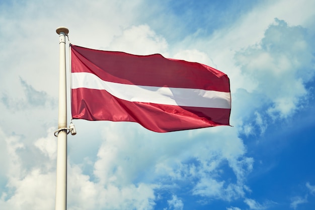 Nationale vlag van Letland op vlaggestok tegen bewolkte hemel