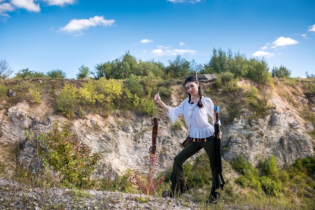 Native American female holding bow and arrow posing at nature