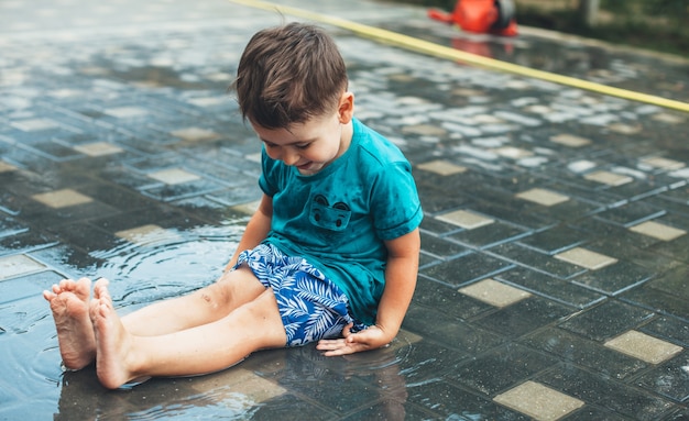 Natte blanke jongen spelen in de tuin met water zittend op de grond en glimlachen