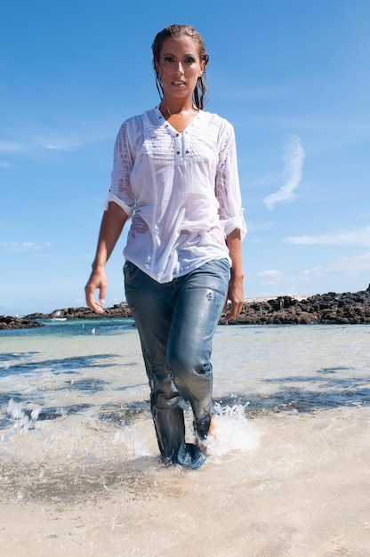 Natte jonge vrouw in kleding aan de kust in de lente of zomer onder een blauwe lucht