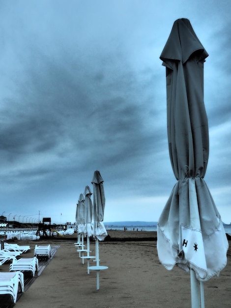 Foto natte ligbedden en parasols op het zeestrand tijdens zware regenstorm opgerolde parasol op het strand tegen donkere bewolkte hemel invasie van een tyfooncycloon of storm op zee of oceaan strandseizoen